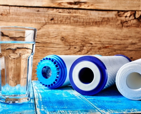 Household water filtration system. Carbon filters and a glass of water on a table.